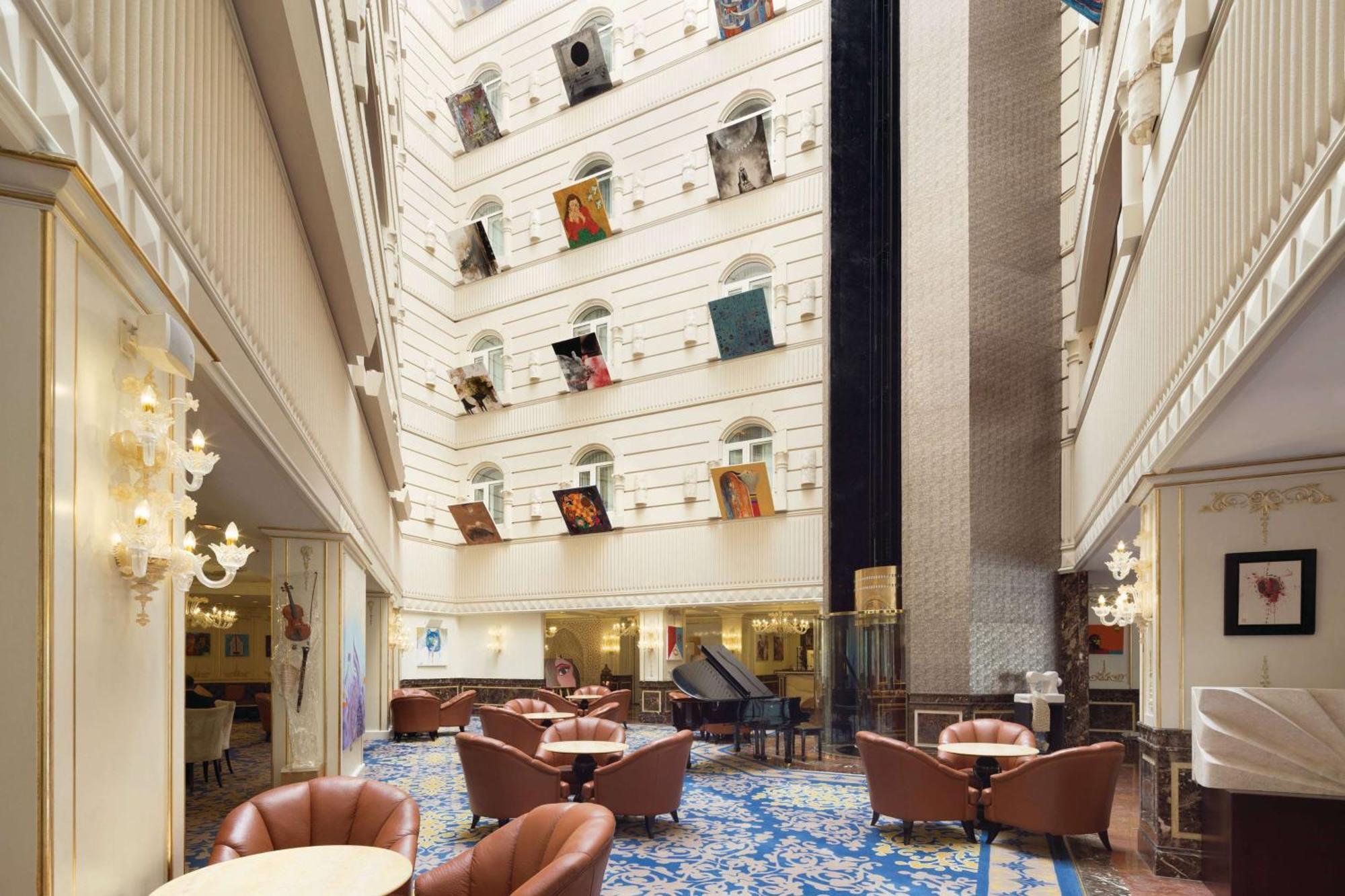 Grand Regency Doha, Trademark Collection By Wyndham Экстерьер фото The photo depicts the interior of a spacious, upscale hotel lobby. The design features high ceilings and multiple levels, with large windows that create a bright and airy atmosphere. Elegant light fixtures adorn the walls, and the floor is covered wi