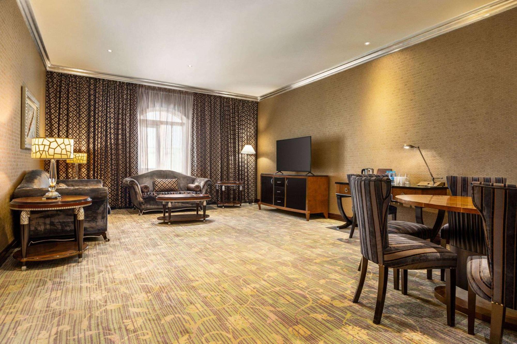 Grand Regency Doha, Trademark Collection By Wyndham Экстерьер фото The photo shows a spacious lounge or living area. It features a comfortable seating arrangement with a dark-colored sofa and armchairs, arranged around a coffee table. There's a dining table with matching chairs, suggesting it can accommodate meals o